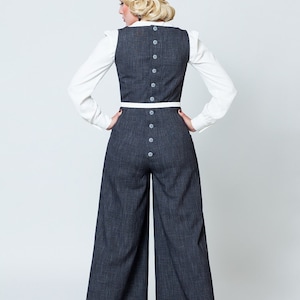 May include: A woman wearing a dark gray wide-leg jumpsuit with a white trim and button detailing on the back. She is wearing a white blouse underneath the jumpsuit.
