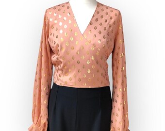May include: A peach-colored blouse with a V-neck and long sleeves. The blouse has a gold leaf pattern.