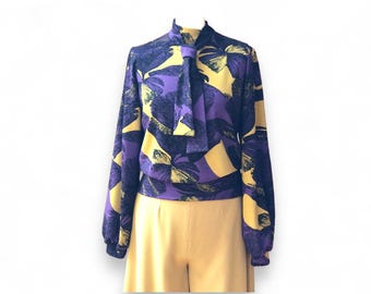 May include: A long-sleeved blouse with a high neck and a tie at the neck. The blouse has a purple and yellow floral pattern.