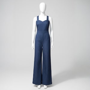 Könnte beinhalten: Dunkelblauer Jeans-Jumpsuit mit weitem Bein und herzförmigem Ausschnitt. Der Jumpsuit hat zwei Vordertaschen und Knopfdetails an den Trägern. Das Kleidungsstück wird auf einer Schaufensterpuppe vor weißem Hintergrund präsentiert.