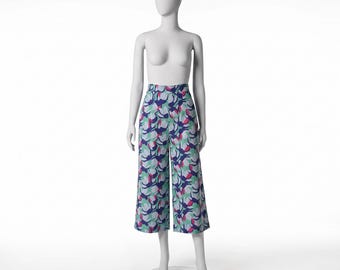May include: High-waisted wide-leg trousers featuring a repeating abstract floral pattern in shades of dark blue, light mint green, and vibrant magenta on a white background, displayed on a mannequin to show the cropped length and fit.