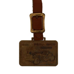 May include: A vintage brown leather luggage tag with a brass buckle and a rectangular brass plate. The plate features an embossed image of construction equipment and the text "Michigan Hancock Signature".