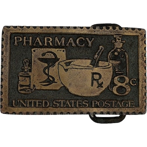 Może przedstawiać: Prostokątna, brązowa klamra do paska z napisem "PHARMACY" na górze. Klamra przedstawia obrazy związane z apteką, w tym moździerz i tłuczek, kaduceusz i butelkę. Słowa "UNITED STATES POSTAGE" znajdują się na dole.