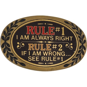 Puede incluir: Una hebilla de cinturón ovalada con un borde dorado y un centro negro. El texto "RULE #1 I AM ALWAYS RIGHT RULE #2 IF I AM WRONG... SEE RULE #1" se muestra en letras rojas y doradas.