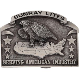 May include: A silver-toned metal belt buckle featuring an eagle perched atop a map of the United States. The buckle has the text "SUNRAY LITES" at the top and "SERVING AMERICAN INDUSTRY" at the bottom, with stars on either side.