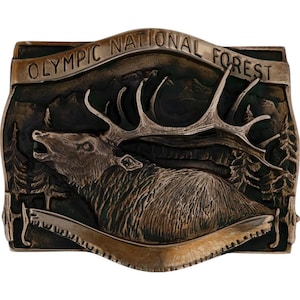 May include: A bronze-toned metal belt buckle featuring a detailed relief of an elk with large antlers, set against a backdrop of mountains and trees. The words "OLYMPIC NATIONAL FOREST" are arched across the top. The buckle has a rectangular shape.