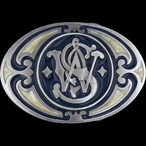 以下が含まれることがあります： 楕円形のシルバーのベルトバックル。ネイビーブルーの中央に「S W A」の文字がスタイリッシュにデザインされています。 バックルはクリーム色の縁取りと装飾的なシルバーのアクセントがあり、黒い背景に配置されています。