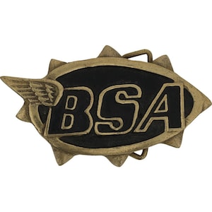 May include: A vintage-style belt buckle with the letters "BSA" in gold against a black background. The buckle has a gold-colored sunburst design around the edges and a wing emblem on the left side. The buckle is made of metal.