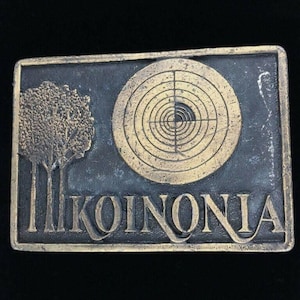May include: A brass belt buckle with a gold-colored target and the word "KOINONIA" in a stylized font.