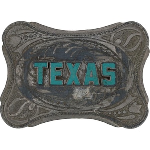 Può includere: Fibbia per cintura rettangolare color argento con la scritta "TEXAS" in lettere turchesi. La fibbia presenta un bordo ornato, simile a un motivo floreale. Lo sfondo della fibbia ha un aspetto usurato e invecchiato.