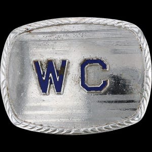 May include: Silver-toned rectangular belt buckle with the letters "WC" in blue enamel. The buckle has a textured, striped background and a decorative rope-like border. The letters are outlined in a darker blue.