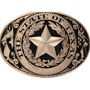 May include: Oval-shaped belt buckle with a bronze finish. The buckle features a large star in the center, surrounded by the words "THE STATE OF TEXAS" and decorative elements. The design is detailed and embossed.