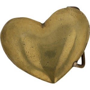 May include: A vintage brass heart-shaped belt buckle. The buckle has a tarnished, aged appearance, with a slightly textured surface. The heart shape is prominent, and the buckle hardware is visible on the back.