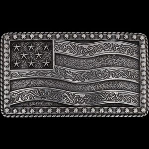 May include: A rectangular silver-colored belt buckle featuring an engraved American flag design. The flag includes stars and stripes with ornate floral scrollwork. The buckle has a rope-like border.