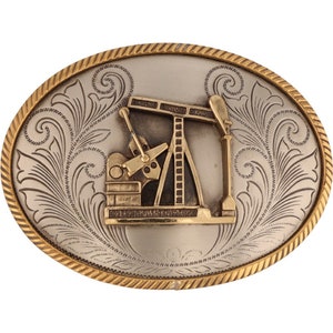 Può includere: Fibbia per cintura ovale in argento e oro con un design inciso di una piattaforma petrolifera.