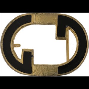 May include: An oval-shaped belt buckle with a gold-colored frame and a black enamel inlay. The design features a stylized double-G logo. The buckle has a vintage appearance with a cracked finish.