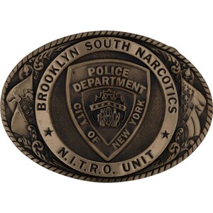Puede incluir: Hebilla de cinturón ovalada de bronce con el texto "BROOKLYN SOUTH NARCOTICS" y "N.I.T.R.O. UNIT". El centro muestra un escudo con "POLICE DEPARTMENT CITY OF NEW YORK".