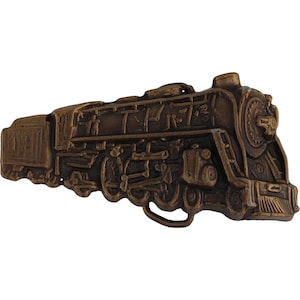 May include: A vintage brass belt buckle featuring a detailed design of a steam locomotive. The buckle is a dark brown color and has a realistic depiction of the train.