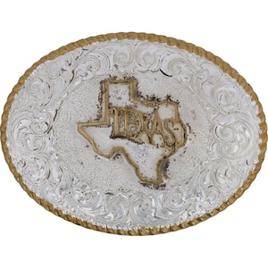 Peut inclure: Boucle de ceinture ovale argentée avec un contour doré du Texas et le mot "TEXAS" en or. La boucle présente un motif orné de volutes et une bordure dorée en forme de corde.