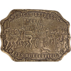 Puede incluir: Hebilla de cinturón de latón vintage con un diseño en relieve que representa una diligencia tirada por caballos. La hebilla es rectangular con bordes redondeados e incluye el texto "AMERICAN EXPRESS CO" y "WELLS BUTTERFIELD & CO".