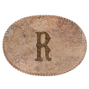 May include: Oval silver-coloured belt buckle with a decorative rope-like border. The buckle features an embossed floral pattern and a gold-coloured letter "R" in the centre. Designed for a belt.