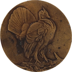 May include: A circular, bronze-colored relief sculpture featuring a detailed depiction of a bird, possibly a grouse or pheasant. The bird is shown in profile, with its tail feathers fanned out. The artwork has a textured surface.