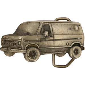 May include: A vintage-style metal belt buckle shaped like a van. The buckle is a dull silver color with detailed features, including wheels, windows, and a roof rack. The van appears aged, with a textured surface.
