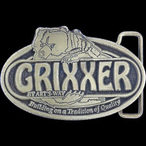 Könnte beinhalten: Vintage Gürtelschnalle aus Messing mit dem Wort "Grixxer" in einem kühnen, ovalen Design. Die Schnalle zeigt eine Bär-Grafik und den Text "By Art's Way" und "Building on a Tradition of Quality". Die Schnalle hat eine rechteckige Schlaufe.
