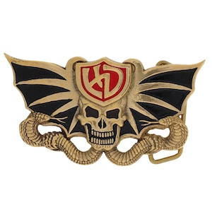 May include: A gold-colored metal belt buckle featuring a skull, wings, and two snakes. The buckle has a red and gold shield in the center with a stylized design. The wings are black with gold trim.
