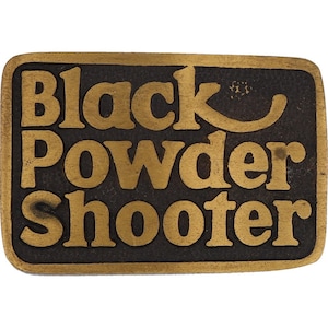 May include: A gold-colored metal belt buckle with the words "Black Powder Shooter" in raised lettering.