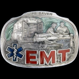 Puede incluir: Hebilla de cinturón EMT plateada con un diseño en relieve detallado. Presenta una ambulancia, personal médico y las palabras "LIFE SAVER" y "EMT". El símbolo de la Estrella de la Vida es azul y rojo.
