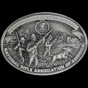 May include: A silver belt buckle with a detailed image of three hunters with rifles and a dog in a field. The buckle is oval shaped and has the text "Preserving Our Hunting Heritage National Rifle Association of America" around the edge. The National Rifle Association logo is in the center of the buckle.