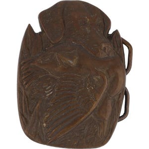 May include: A bronze belt buckle featuring a detailed relief sculpture of a dog pointing its nose at a bird with its wings spread. The buckle is oval shaped and has a textured surface.