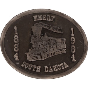 May include: A silver-toned metal belt buckle with a train engine design. The buckle features the text "EMERY 1884 1984 SOUTH DAKOTA".