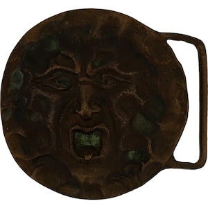 May include: A vintage, round belt buckle with a distressed bronze finish. The buckle features a sculpted face with an open mouth and detailed facial features. The metal has areas of green oxidation.