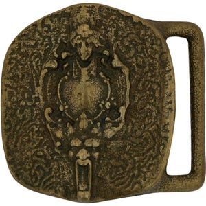 May include: A vintage brass belt buckle with an oval shape. The buckle features a detailed, embossed design of a heraldic crest with a lion's head at the bottom. The buckle has a rectangular bar for the belt strap.
