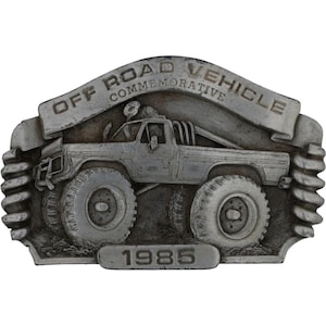 May include: A silver-colored commemorative plaque featuring an off-road vehicle. The plaque has the text "OFF ROAD VEHICLE COMMEMORATIVE" and the year "1985". The vehicle has large tires and a roll bar.