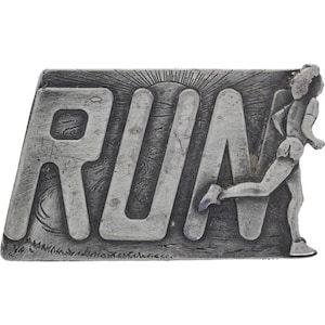 May include: A silver-coloured belt buckle with the word "RUN" in large letters. A runner is shown on the right, with a sunburst design behind. The buckle has a textured, vintage look.