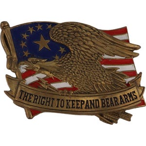 Puede incluir: Un emblema metálico color latón con un águila con las alas extendidas, una bandera y el texto "THE RIGHT TO KEEP AND BEAR ARMS". La bandera tiene rayas rojas y blancas y un campo azul con estrellas. El emblema es rectangular.