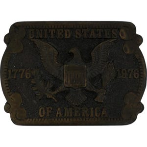 May include: A rectangular, bronze-colored belt buckle featuring the words "UNITED STATES OF AMERICA" and the years "1776" and "1976." The central design includes an eagle with outstretched wings, holding a shield and olive branch.