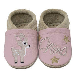 Pode incluir: Sapatos de beb&eacute; cor-de-rosa com um veado e estrelas bordadas. Os sapatos s&atilde;o personalizados com o nome "Nina".