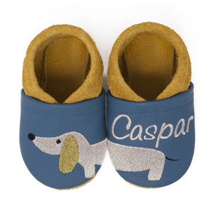 May include: A pair of blue leather baby shoes with a dachshund design and the name "Caspar" embroidered on the right shoe.