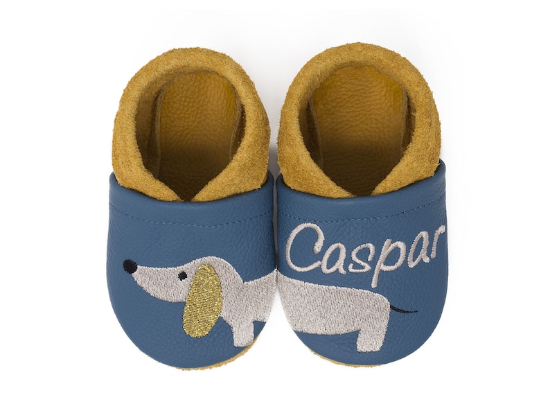 May include: A pair of blue leather baby shoes with a dachshund design and the name "Caspar" embroidered on the right shoe.
