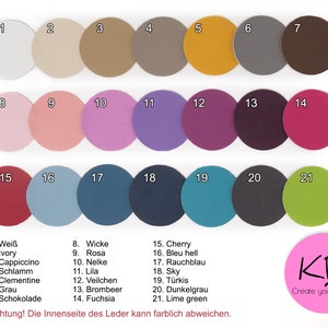 May include: A chart of 21 different colored leather swatches, numbered 1 through 21. Each swatch is a circle with a number in the center. The swatches are arranged in three rows of seven. The colors include white, ivory, cappuccino, brown, mustard yellow, gray, dark brown, pink, light pink, purple, lavender, burgundy, dark purple, red, light blue, dark blue, teal, dark gray, green, and lime green. The text "Achtung! Die Innenseite des Leder kann farblich abweichen." is at the bottom of the chart. The text "KB Create your Cover" is in a pink circle at the bottom right of the chart.