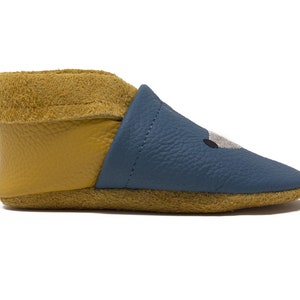 May include: Blue leather baby booties with a yellow fold-over cuff and a stitched animal face design.