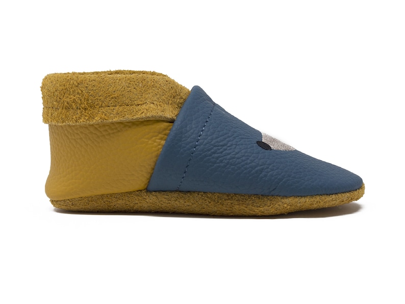 May include: Blue leather baby booties with a yellow fold-over cuff and a stitched animal face design.