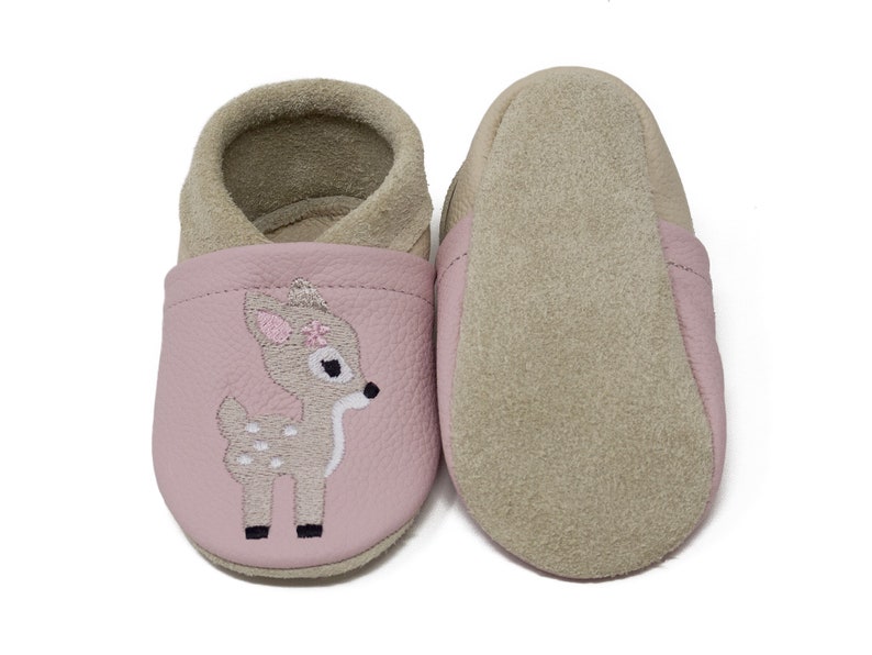 Pode incluir: Sapatos de beb&eacute; de couro rosa com um veado marrom bordado na frente. Os sapatos t&ecirc;m um forro de camur&ccedil;a e uma sola macia.