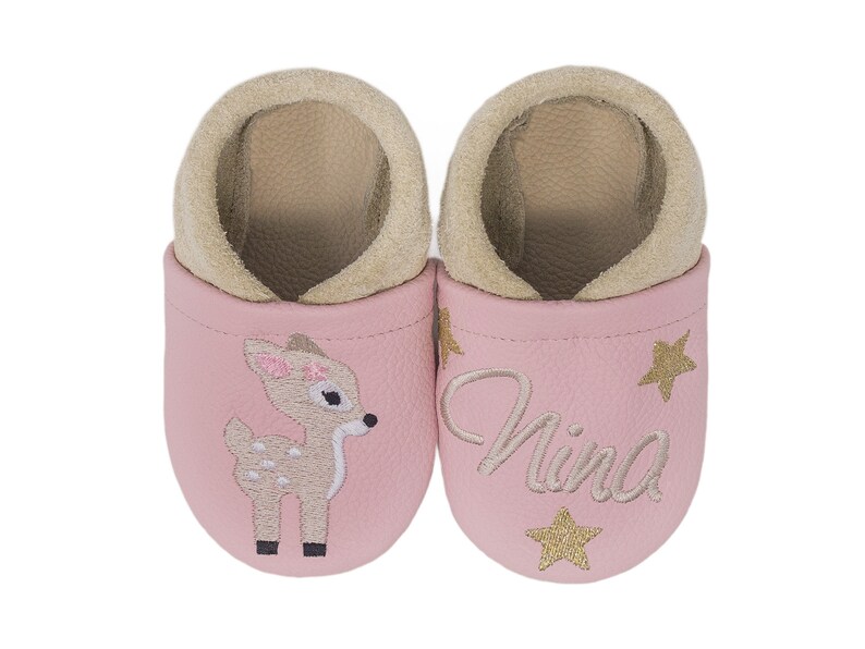 Pode incluir: Sapatos de beb&eacute; de couro rosa com um veado e estrelas douradas bordadas. Os sapatos dizem "Nina" em um deles.
