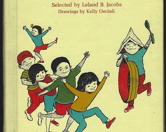 Può includere: Un libro con copertina rigida intitolato Playtime in the City, selezionato da Leland B. Jacobs con disegni di Kelly Oechsli. La copertina giallo pallido presenta un'illustrazione colorata di sei bambini che giocano, uno indossa un cappello di giornale.