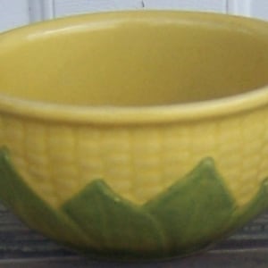 May include: A yellow ceramic bowl with a corn cob design. The bowl has a textured exterior and green leaf-shaped accents at the base. The interior is smooth and the bowl is suitable for serving food.
